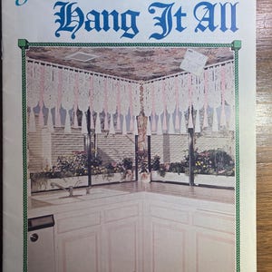 May include: A vintage book cover titled "Juliano's Hang It All" with a green border. The image shows a kitchen corner with white cabinets, a sink, and a window with floral arrangements. The text "Sweet and Sassy" is at the bottom.