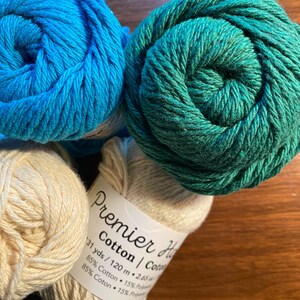 May include: Three balls of yarn in different colors: teal, light blue, and cream. The cream ball has a label that reads "Premier Cotton | Cotton 131 yds / 120 m 2.65 oz 85% Cotton 15% Polyester 85% Coton 15% Polyester."