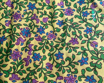 May include: A yellow fabric with a repeating pattern of green vines and purple and blue flowers.