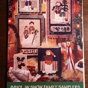 May include: A set of four framed cross-stitch patterns featuring a snow family. The patterns are titled "88101 JW Snow Family Samplers" and "Fiber Mosaics".