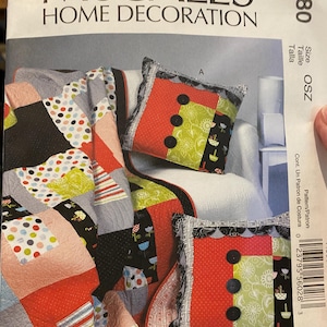 May include: McCall's Home Decoration pattern featuring a colorful patchwork quilt and two decorative pillows. The pillows have red, green, and black fabric with large black buttons. The quilt has a variety of patterns and colors.
