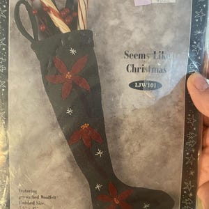 May include: A black Christmas stocking with red poinsettias and white star accents. The stocking is filled with candy canes and berries. The text "Seems Like Christmas" is visible. Finished size is 5.5" x 15".