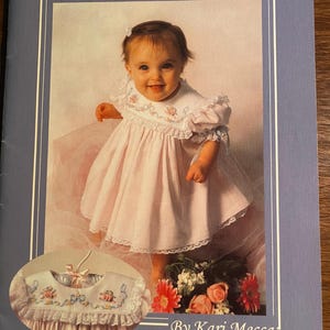 May include: A book cover with a light blue background featuring a photo of a baby girl wearing a white dress with pink and white embroidery. The title of the book is "Silk Ribbon Whimsy" and the author is "By Kari Mecca".