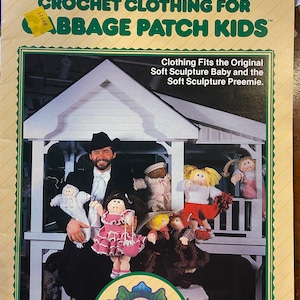 May include: A crochet clothing pattern book for Cabbage Patch Kids dolls. The cover features a man in a suit holding a Cabbage Patch Kid doll. The book is titled "Crochet Clothing for Cabbage Patch Kids" and has a plaid pattern on the back cover.