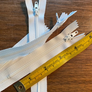 May include: Three white zipper closures with a yellow measuring tape. The tape reads "FIBER-GLASS MADE IN CHINA" and measures up to 30 cm.