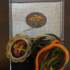 Puede incluir: Un kit de punto de cruz con un diseño de árbol marrón, naranja y amarillo. El kit incluye una aguja, hilo de bordar en naranja, verde y marrón, y un lienzo preimpreso.