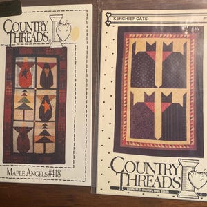 May include: Two quilting patterns from Country Threads. The first pattern is called "Maple Angels" and features a quilt block with a red, white, and black color scheme. The second pattern is called "Kerchief Cats" and features a quilt block with a black, white, and purple color scheme.