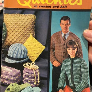 May include: A vintage crochet and knit pattern book titled "Quickies" by Coats & Clark's. The book cover features a photo of two people wearing crocheted garments, a woman in a blue and green cardigan and a man in a brown cardigan. The book cover also features a variety of crocheted items, including a cushion, a hat, a bag, and slippers.