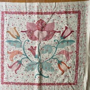 Puede incluir: Un trozo cuadrado de tela con un diseño floral. La tela es blanca con un patrón floral rosa, naranja y verde. La tela está rodeada por un borde rojo.