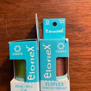 Op de afbeelding: Twee spoelen Coats Eloflex Stretch-garen, een groene en een bruine, elk met 225 yards (205 meter) garen. De verpakking is blauw en wit met het Coats-logo en de tekst "It Stretches!" en "Stretch Thread".