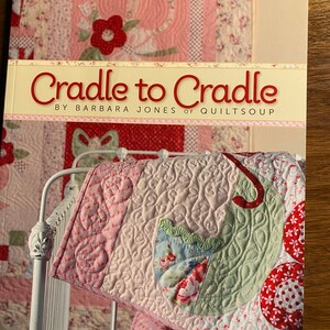 May include: A book titled "Cradle to Cradle" by Barbara Jones of Quiltsoup. The cover features a pink and green quilt with a floral design.