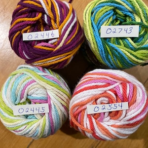 May include: Four balls of yarn in different color combinations. The yarn is striped with white, pink, orange, yellow, green, blue, and purple. Each ball has a handwritten label with a number: 02446, 02743, 02445, and 02354.