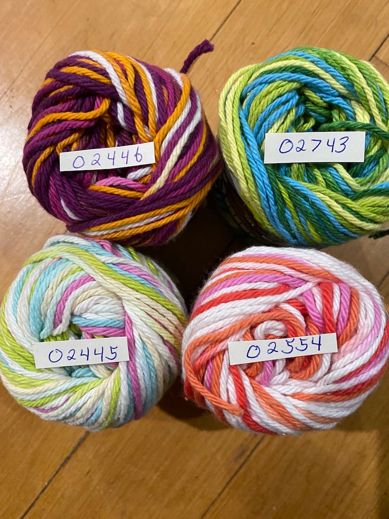 May include: Four balls of yarn in different color combinations. The yarn is striped with white, pink, orange, yellow, green, blue, and purple. Each ball has a handwritten label with a number: 02446, 02743, 02445, and 02354.