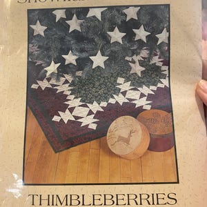 May include: A package for a Snowflake Tree Skirt by Thimbleberries. The design features a Christmas tree with star ornaments and a burgundy and white snowflake pattern. Two wooden decorative items are also visible.