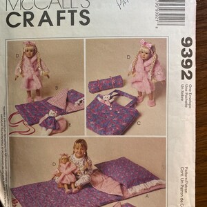 May include: A McCall's Crafts sewing pattern envelope numbered 9392 featuring illustrations of a doll wearing a pink robe and slippers, a sleeping bag, a pillow, a tote bag, and a small stuffed cat toy with a pink and blue floral fabric pattern.