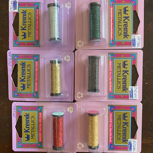 May include: Six spools of Kreinik metallic thread in various colors, including silver, green, gold, red, and gold. Each spool is labeled "Kreinik Metallics" and "BALGER Very Fine (#4) Braid".