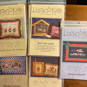 Puede incluir: Cuatro patrones de punto de cruz con temas navideños de invierno. Los patrones se titulan "Hearts Warm at Christmas", "Gift of Love", "Noah's Noel" y "Peace on Earth".