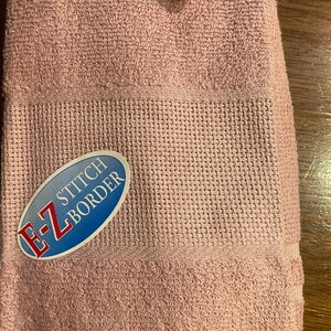 May include: A pink towel with a blue and white label that says "E-Z STITCH BORDER".