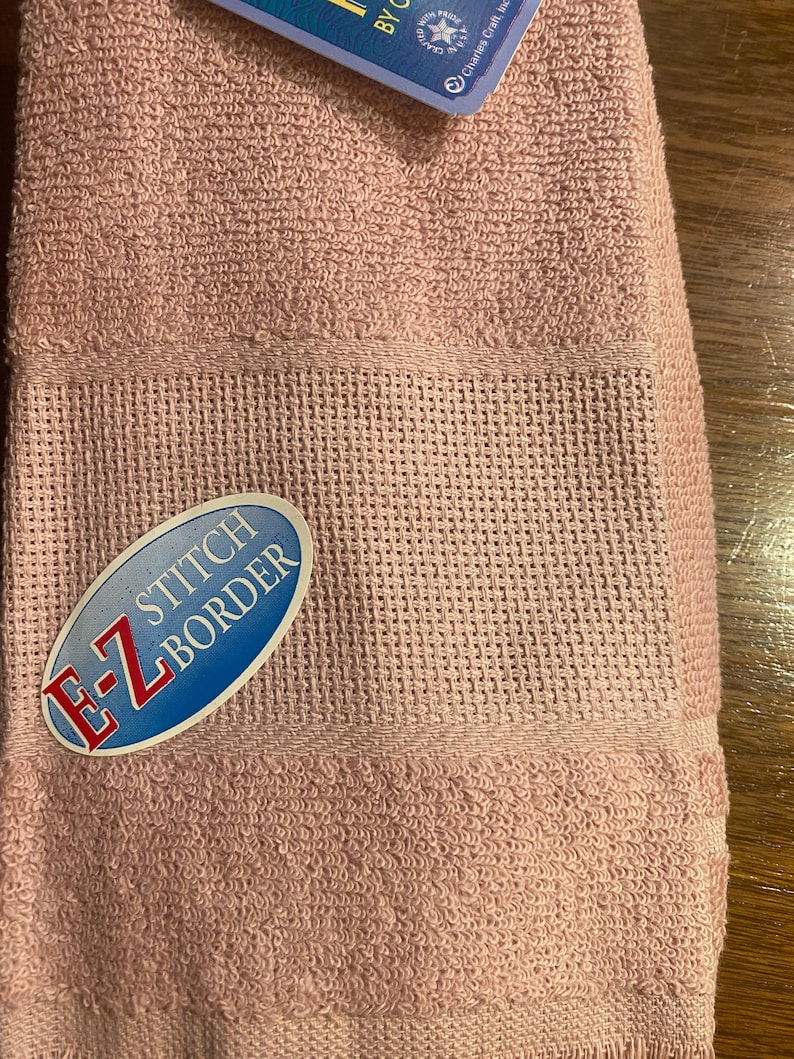 May include: A pink towel with a blue and white label that says "E-Z STITCH BORDER".