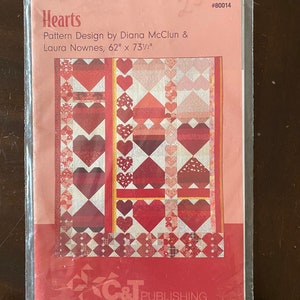 May include: A quilting pattern for a quilt called "Hearts" designed by Diana McClun & Laura Nownes. The quilt is 157 cm by 187 cm and features a red, white, and pink colour scheme with a heart pattern.