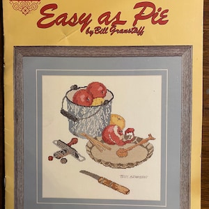 Può includere: Schema di punto croce per una natura morta con una ciotola di mele, un piatto per torte, un coltello e un cucchiaio. Il modello è intitolato "Easy as Pie" di Bill Granstaff.