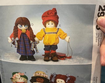 May include: A vintage McCall's Crafts sewing pattern for making five different dolls. The pattern cover features illustrations of the dolls, including a girl with glasses, a girl with a red hat, a girl with a straw hat, a girl with a red bow, and a girl with a red and white dress. The pattern number is 298.