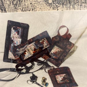 May include: A collection of quilting supplies, including small fabric squares, scissors, thimbles, and ribbon. The fabric pieces feature a patchwork design with a dark paisley pattern. The items are arranged on a white surface.