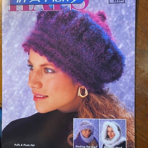 May include: A magazine cover featuring a woman wearing a purple and pink fuzzy hat. The magazine is titled "Hats In A Hurry" and is published by Annie's Attic. The cover also shows three different hats: a purple and pink fuzzy hat, a white crocheted hat with a matching scarf, and a white marabou feather hat.