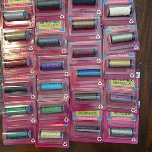 May include: A collection of 18 spools of Kreinik metallic embroidery floss in various colors. The spools are labeled "Kreinik Metallics" and "Balger Fine 100% Braid".