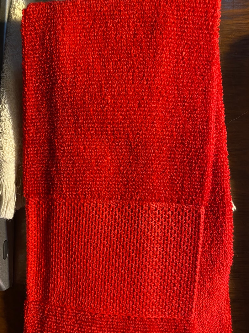 May include: A red terry cloth towel with a smaller red terry cloth square sewn onto the bottom right corner.