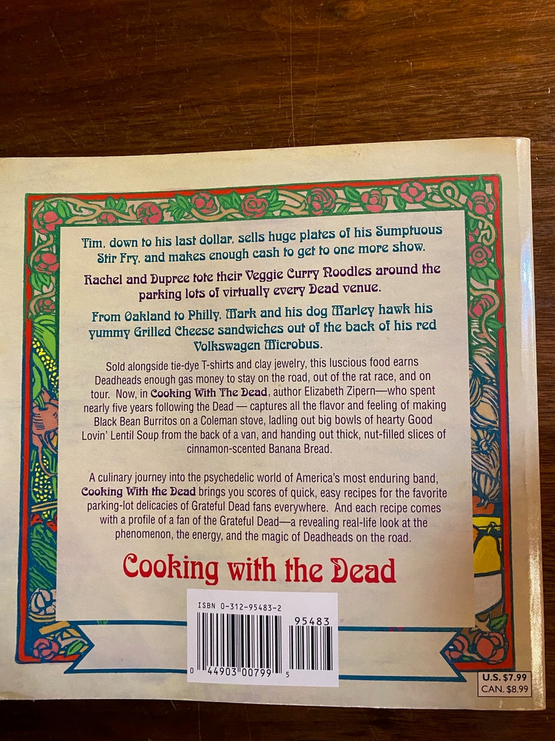 Puede incluir: La contraportada de un libro de bolsillo titulado "Cooking with the Dead" con un borde floral colorido. El libro presenta un c&oacute;digo de barras en blanco y negro y el texto "ISBN 0-312-95483-2". El libro trata sobre los Grateful Dead y presenta recetas de comida que se vend&iacute;a en sus conciertos.