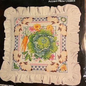 Puede incluir: Un patrón de punto de cruz Bucilla Home Decor collection para una almohada con un huerto con una col, zanahorias y dos conejos. El patrón incluye un gráfico multicolor para facilitar la costura. La almohada terminada mide 10 cm por 35,5 cm más un volante.