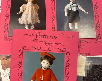 May include: Three doll patterns with images of vintage dolls. The patterns are on pink cardstock with a decorative border and the text "Patterns by Connie Tee Finchum". The dolls are dressed in vintage clothing.