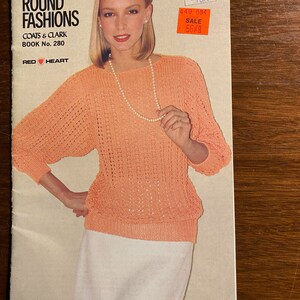 Op de afbeelding: Een vintage magazine cover getiteld "Year Round Fashions" door Coats & Clark, Boek nr. 280, met een vrouw die een perzikkleurige gebreide trui en een witte rok draagt. De cover bevat de tekst "Red Heart".