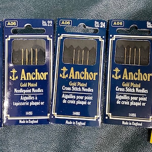 May include: Four packages of gold-plated Anchor needles for needlepoint and cross stitch. The packages are labeled with the size of the needles, which range from 18 to 26.  A package of John James Easy Threading Eye Cross Stitch needles is also shown.