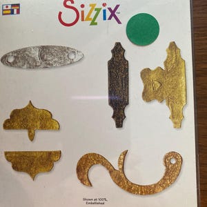 Puede incluir: Un juego de troqueles Sizzix Originals con varias formas metálicas adornadas, incluyendo pestillos y elementos decorativos. El juego incluye un troquel, un punzón y un troquel. El embalaje muestra el logotipo de Sizzix y el texto "Originals".