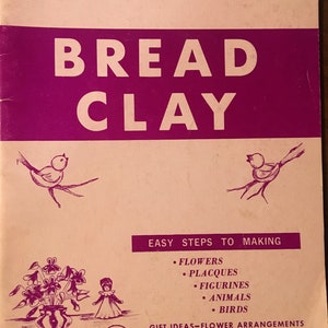 Op de afbeelding: Een roze en witte boekomslag met de titel "BREAD CLAY" in grote, vetgedrukte witte letters. De boekomslag bevat ook de tekst "Ceramics Without Fire" en "EASY STEPS TO MAKING FLOWERS, PLACQUES, FIGURINES, ANIMALS, BIRDS". De boekomslag bevat ook een prijs van $ 1,25.