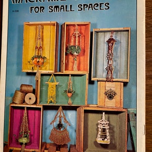 May include: A craft book cover with the title "Macrame' Hangers for Small Spaces". The cover features a colorful display of macrame plant hangers in wooden crates. The book is priced at $1.00.