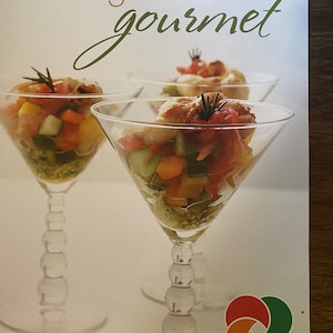 Könnte beinhalten: Ein Kochbuchcover mit dem Titel Ontario Greenhouse Gourmet, das zwei klare Martinigläser mit einem bunten Gemüsesalat zeigt. Der Text lautet Ontario Greenhouse Gourmet und finest in cooking with greenhouse vegetables. In der Ecke befindet sich ein Logo mit vier farbigen Kreisen.