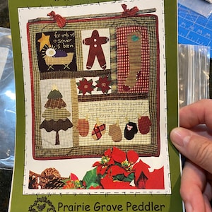 May include: A quilting pattern for a winter-themed wall hanging titled "Seasons Under Heaven - Winter". The pattern features a gingerbread man, a stocking, a Christmas tree, mittens, and a poinsettia. The pattern is 19 inches by 20 inches and is from Prairie Grove Peddler, patterns for the country crafter, #309.
