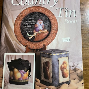 May include: The cover of a book titled "Bob Pennycook's Country Tin Book" features a painted wooden plate with a Santa Claus design. Additional images show a painted teapot and a decorative tin box with teddy bear art.