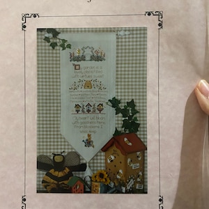 May include: A cross-stitch pattern for a sampler featuring a beehive and the text "My garden is a lovely place, Filled with virtues sweet." and "My heart will bloom with goodness here. From blossoms I shall keep." The pattern is titled "Garden of Virtues" and is by Lorri Birmingham Designs. The finished size is 8 inches wide by 18 inches long.
