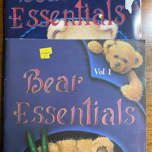 May include: Two books titled "Bear Essentials" are stacked. The top book is labeled "Vol. 3" and the bottom book is labeled "Vol. 1". Both books feature a teddy bear illustration and the title text in a decorative font.