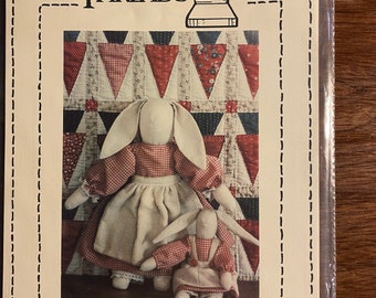 May include: A sewing pattern for making two country-style bunny dolls. The pattern is called "Timeworn Country Rabbits" and is number #110. The pattern features a larger bunny doll wearing a red and white gingham dress and a smaller bunny doll wearing a red and white gingham dress with a white apron.
