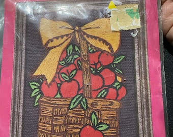 May include: A craft kit for a crewel embroidery picture of a basket of red apples with a yellow bow on top. The kit includes a stamped design on homespun fabric, acrylic crewel yarn, and instructions. The finished piece measures 5 1/2 inches by 6 1/2 inches and fits a 4 1/2 inch by 5 1/2 inch frame.