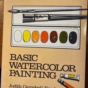 以下が含まれることがあります： ジュディス・キャンベル・リード著「ベーシック・ウォーターカラー・ペインティング」というタイトルの本。表紙には、さまざまな色の水彩絵の具セット、2本の筆、2本の水彩絵の具のチューブが描かれている。