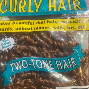 Puede incluir: Un paquete de cabello rizado bicolor, mini-rizos, en tonos marrones. El embalaje muestra las palabras "CURLY HAIR" y "TWO-TONE HAIR". El producto se describe como adecuado para cabello de muñecas, barbas y crines de animales.
