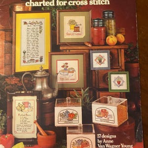 Può includere: Un libro di modelli a punto croce vintage intitolato "Herbs & Spices", con campioni a punto croce incorniciati di erbe, spezie e ricette. La copertina mostra vari progetti a punto croce finiti, tra cui arte incorniciata e contenitori di spezie.