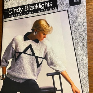 Può includere: Un libretto di modelli di maglia con una donna che indossa un maglione bianco con un motivo geometrico nero. Il libretto è intitolato "Cindy Blacklights Cotton Look - 6 Designs" e ha il numero "1208" e il prezzo "$2.95" sulla copertina.