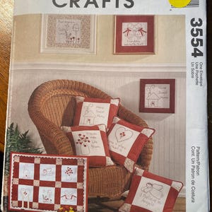 May include: A McCall's Crafts pattern for a quilt with a red and white checkered background and embroidered designs. The designs include a house, a heart, a vase with flowers, and a pair of angels. The pattern number is 3554.